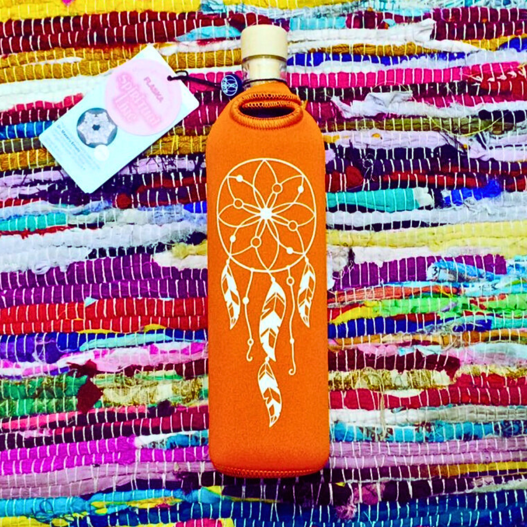 Orange glass water bottle in a neoprene sleeve with a white dreamcatcher design, lying on a colorful woven textile background.